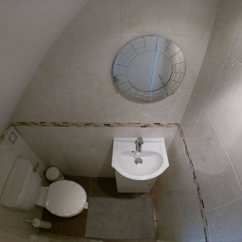 Small bathroom with toilet, sink, round mirror, and tiled walls under a sloped ceiling.