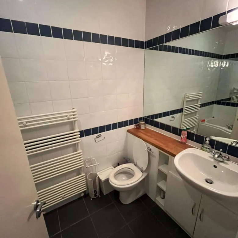 Small bathroom with white tiles, dark blue trim, toilet, sink, and towel rack.