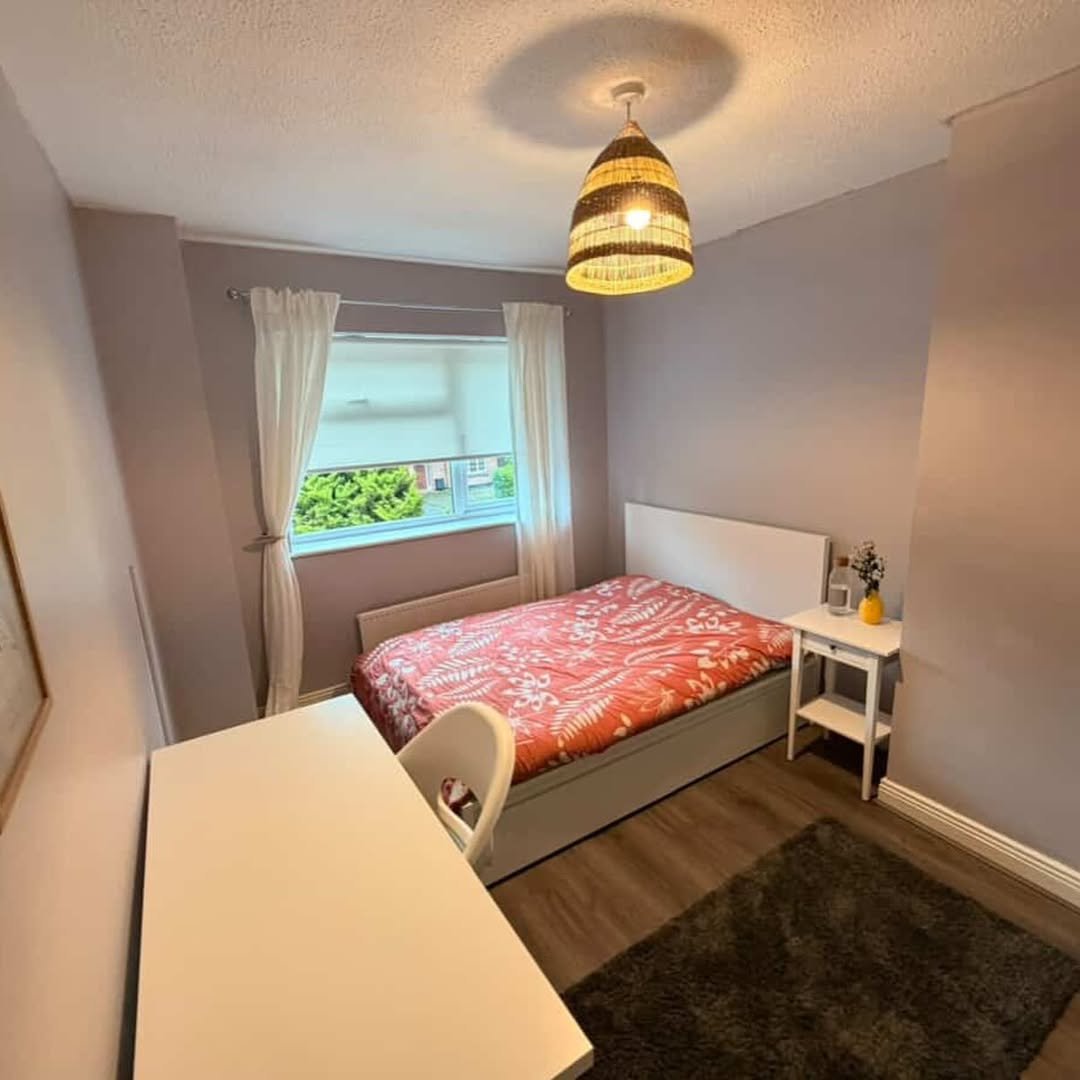 Cozy bedroom with bed, desk, window, and warm lighting.