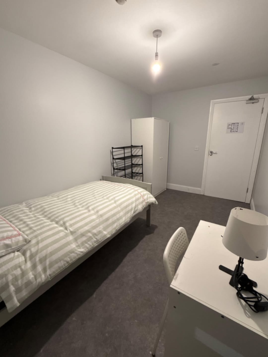 Small bedroom interior with bed, desk, wardrobe, and shoe rack. Neutral decor.