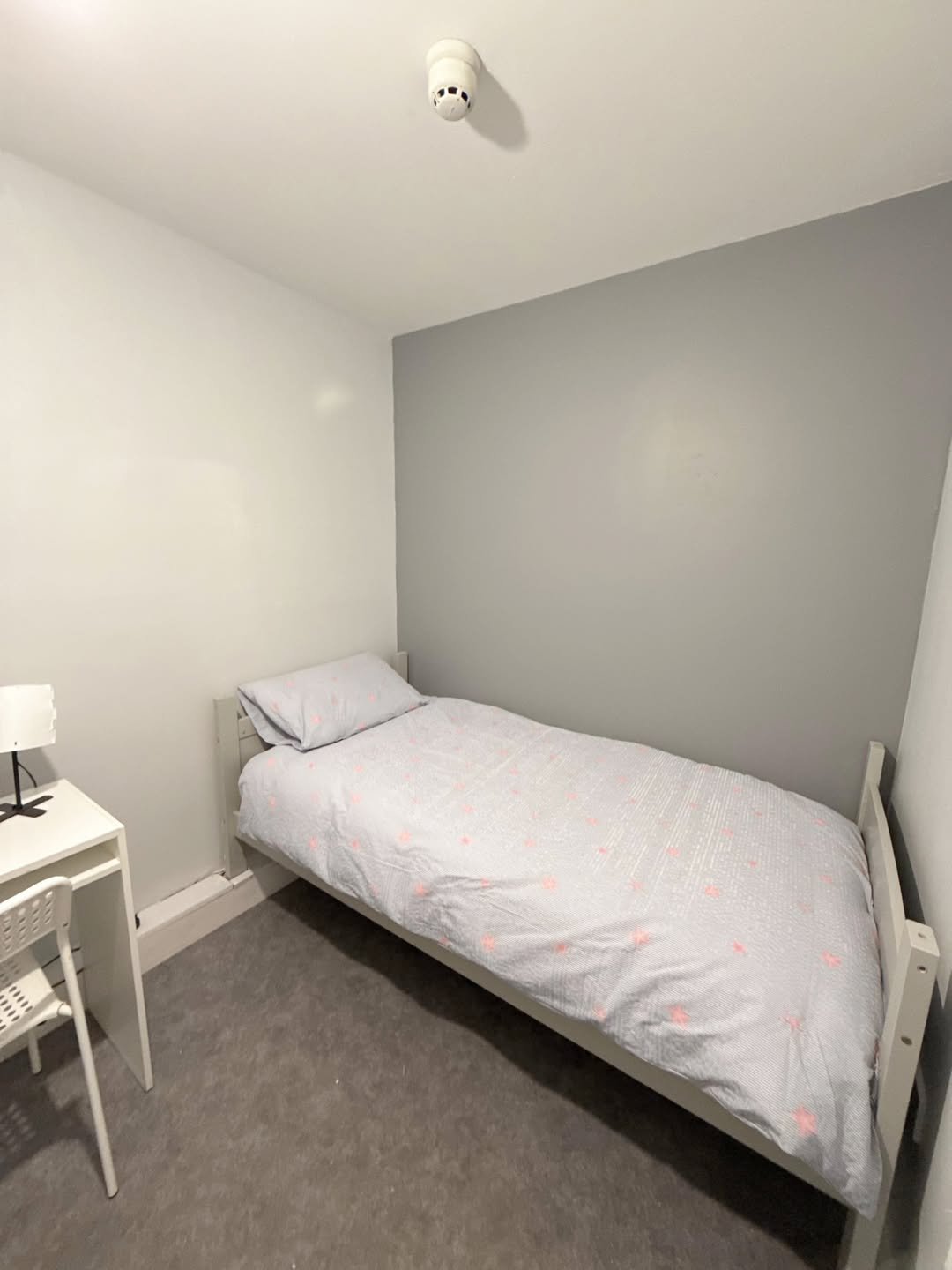 Small bedroom with single bed, desk, and gray/white walls. Minimalist interior design.