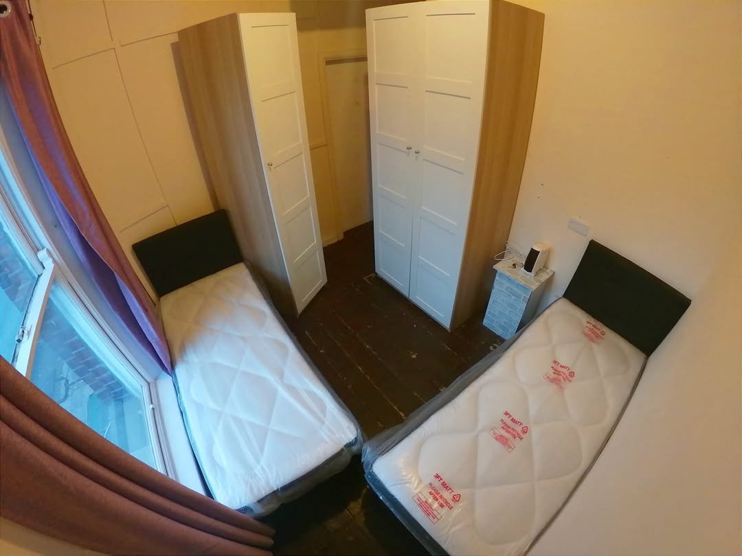 Small bedroom with two twin beds, wardrobes, and window with purple curtains.