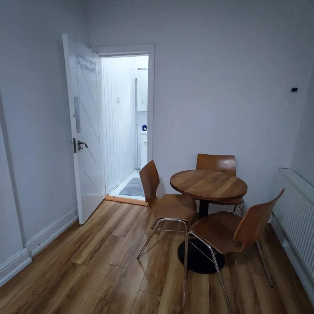 Small dining area with wood table and three chairs next to open bathroom door.