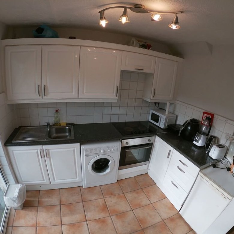 Small kitchen with white cabinets, washing machine, and terracotta floor tiles.