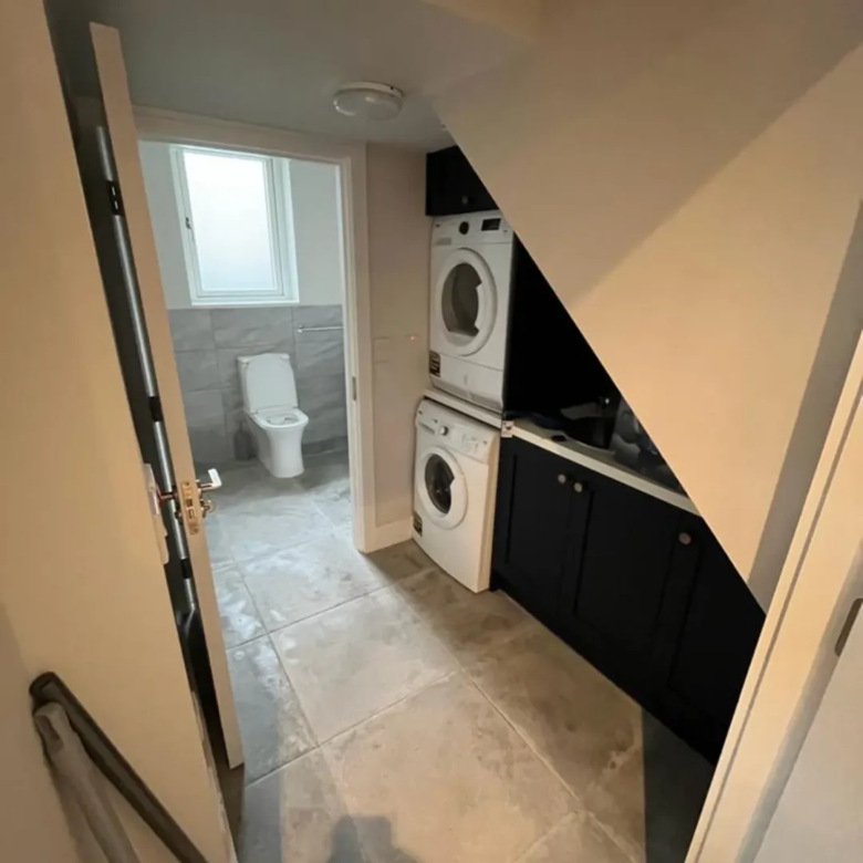 Small laundry room with stacked washer and dryer, dark cabinets, and a view into a tiled bathroom.