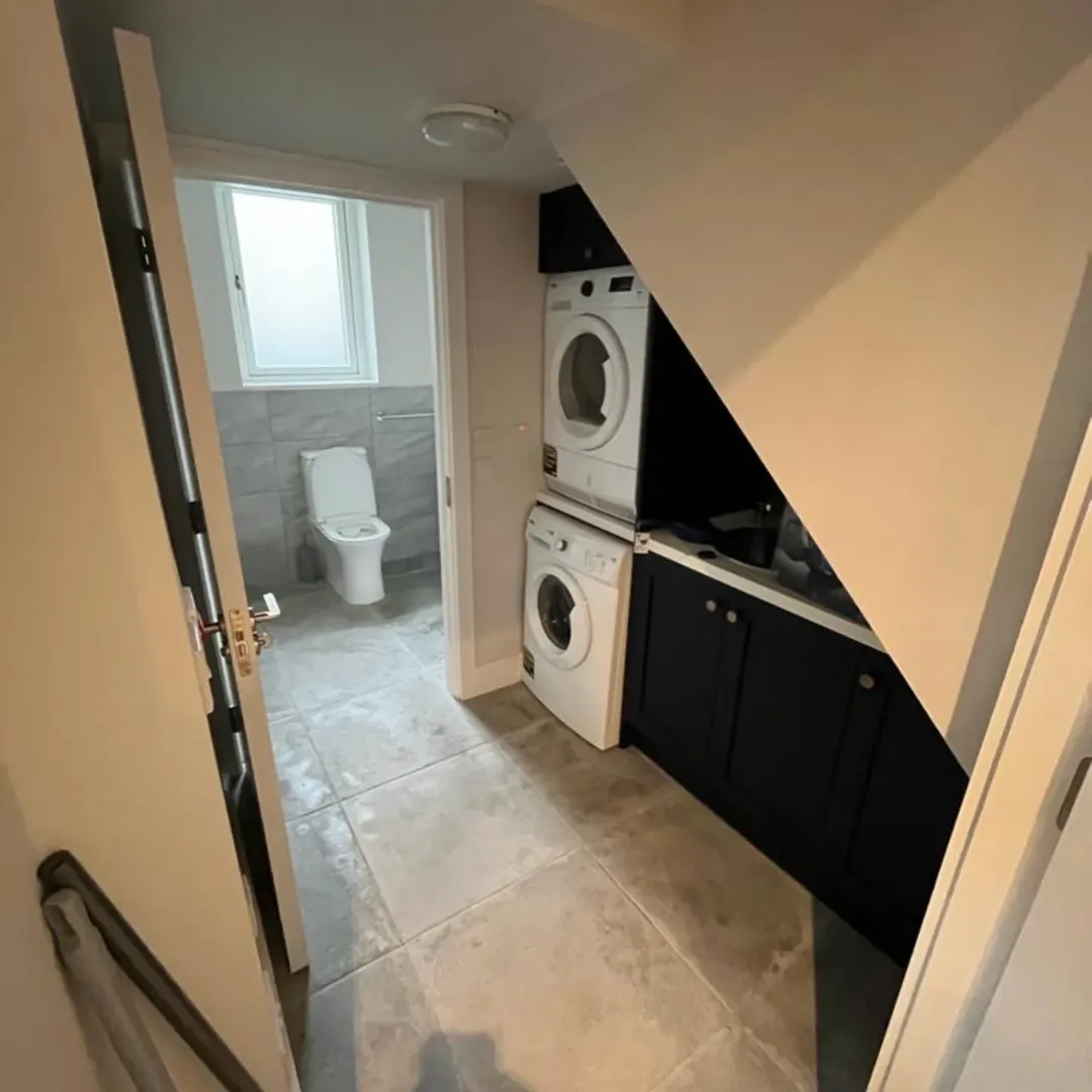 Small laundry room with stacked washer and dryer, dark cabinets, and a view into a tiled bathroom.
