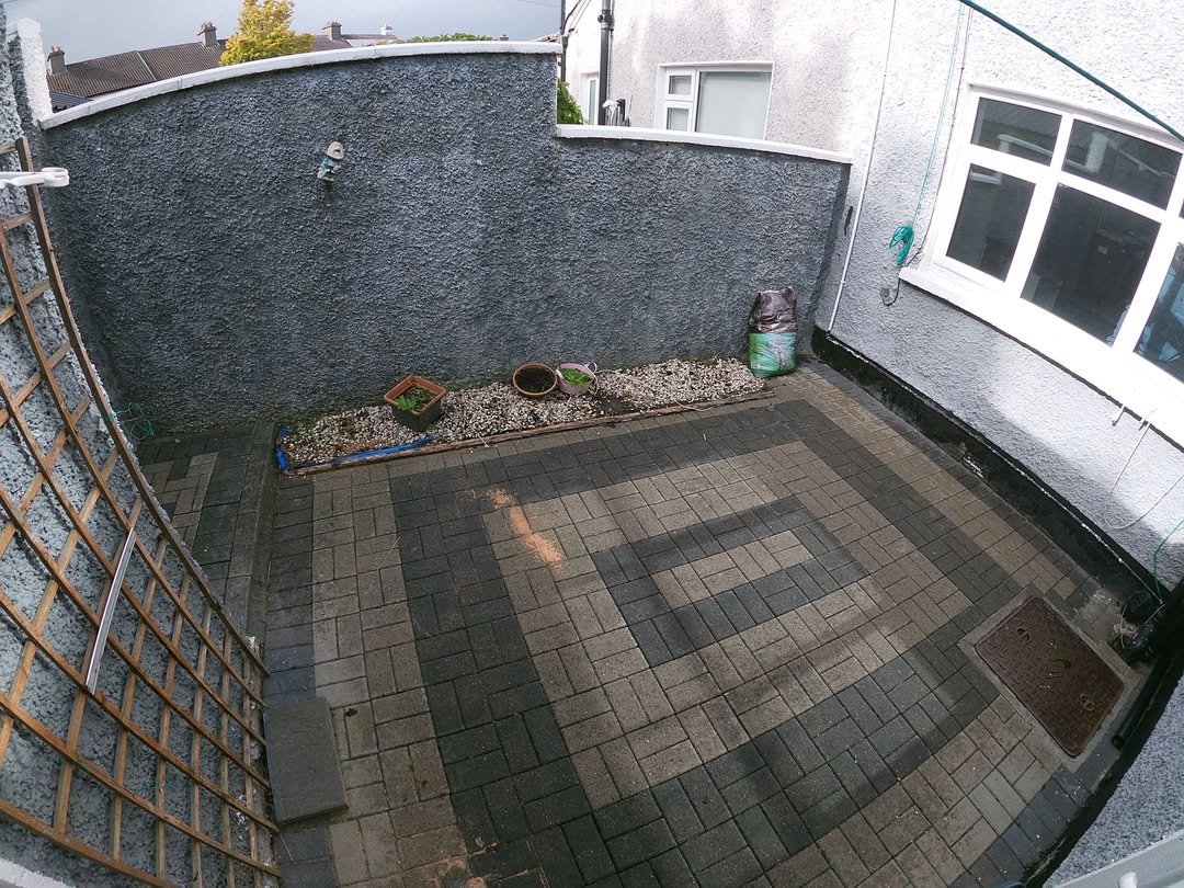 Small paved backyard with patterned brick, wall, and trellis. Plants in pots.
