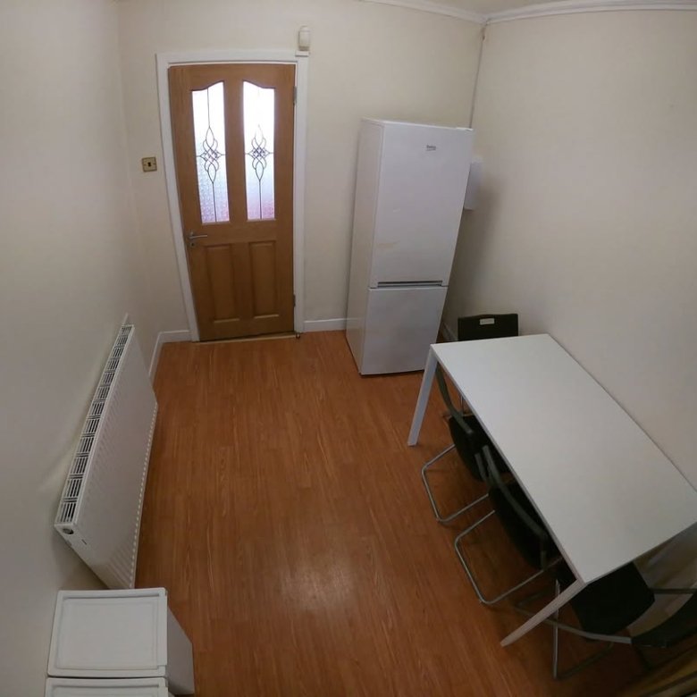 Small room with fridge, table, chairs, and radiator. Neutral tones.