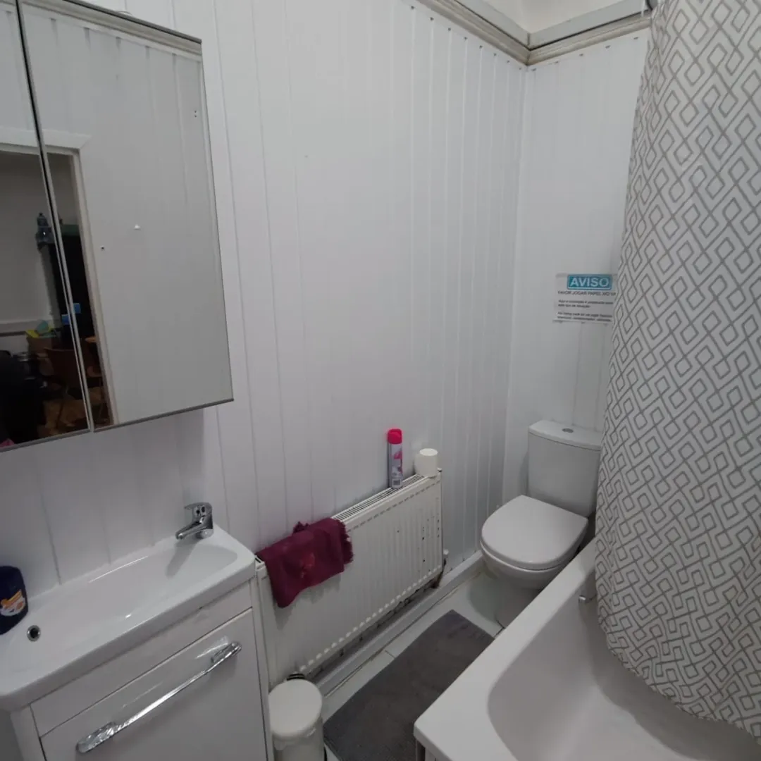 Small bathroom with sink, toilet, and shower curtain. White walls and fixtures.