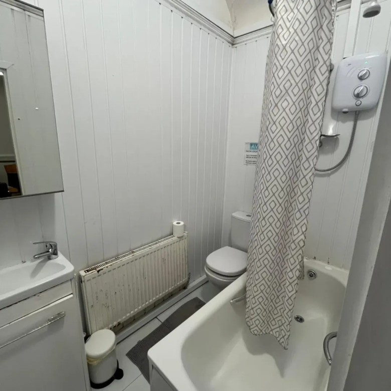 Small bathroom with toilet, bathtub, sink, and radiator. White walls.