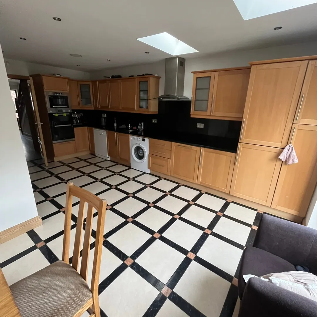 Spacious kitchen with light wood cabinets, black countertops, and checkered tile floor.