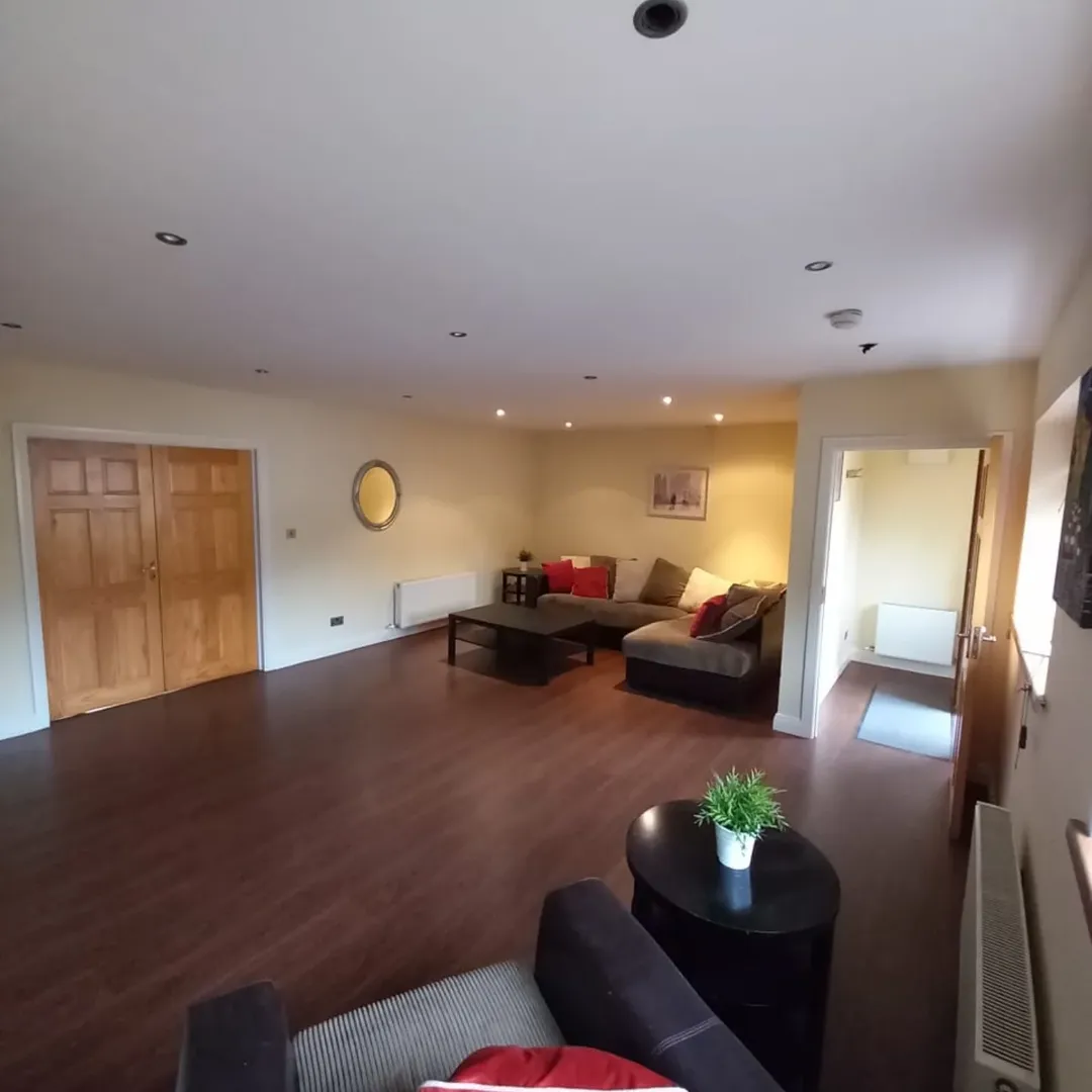Spacious living room with brown sectional sofa, dark wood floors, and a round mirror.
