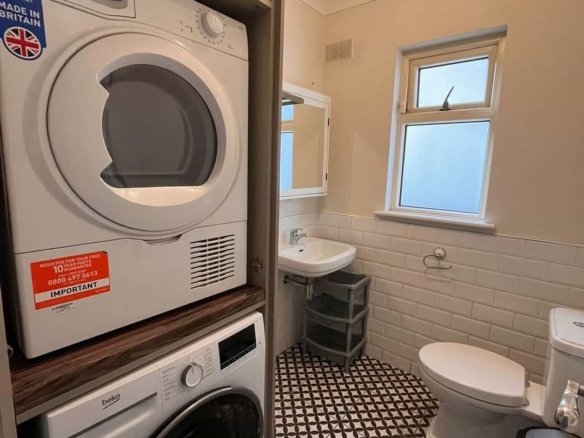 Stacked Indesit dryer and Beko washing machine in a bathroom cabinet.