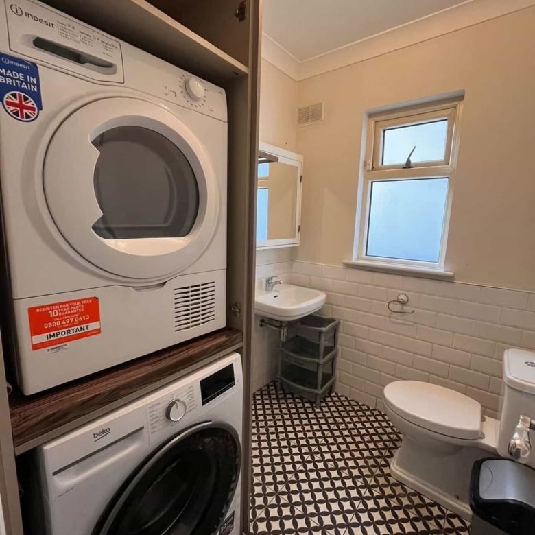 Stacked Indesit dryer and Beko washing machine in a bathroom cabinet.