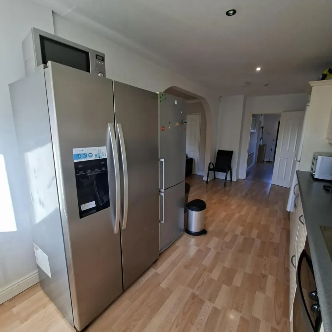 Stainless steel double door refrigerator with water dispenser in kitchen.