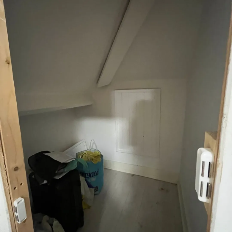 Under stairs storage with bags and items in a small, angled space.