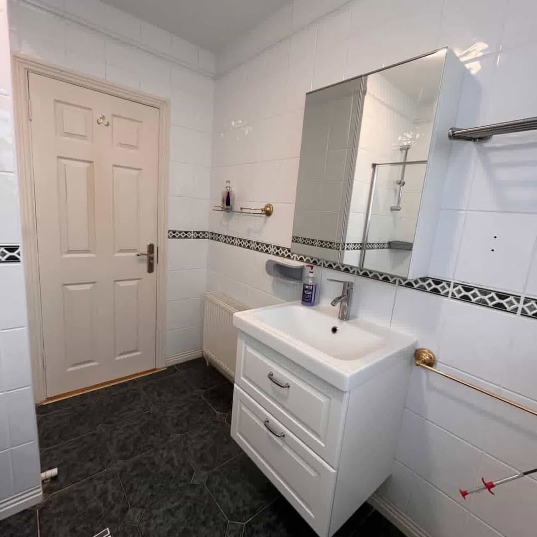 Bathroom with white vanity, mirror cabinet, white tiles, and dark floor. Door on left.