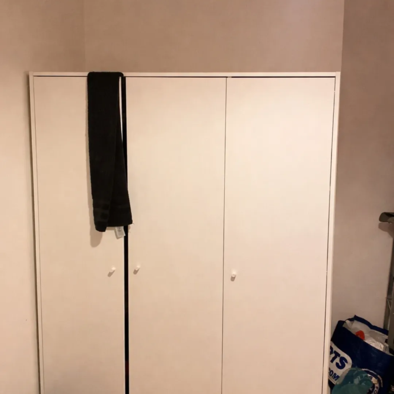 White wardrobe with black scarf hanging on door and shopping bag on floor.
