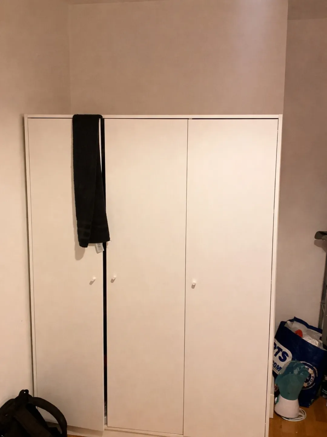 White wardrobe with black scarf hanging on door and shopping bag on floor.