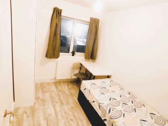A tidy single bedroom with a bed, desk, and wardrobe, featuring light wood flooring and neutral decor. – Ghar.ie property listing