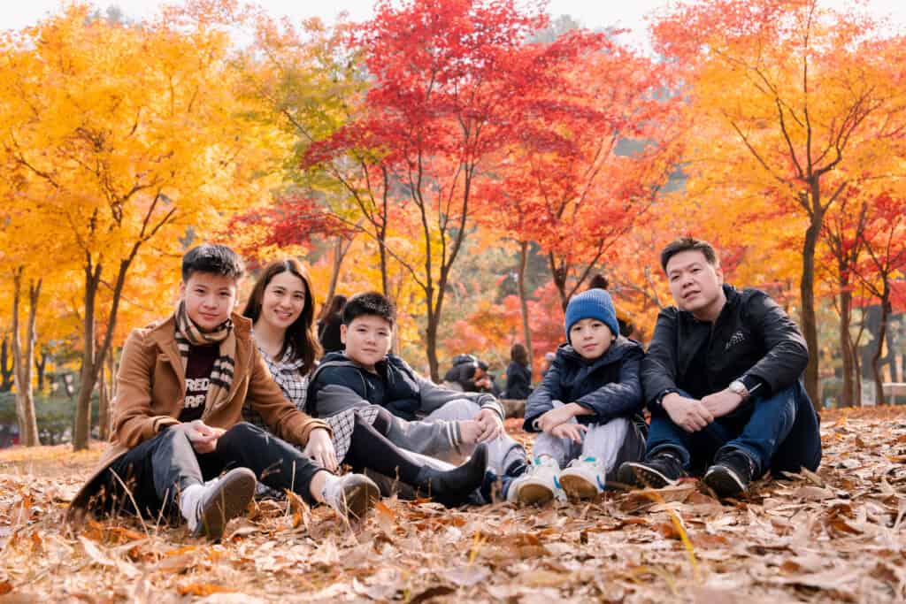 Vibrant fall foliage in Korea captures a family enjoying the autumn scenery amid colorful trees during golden hour.