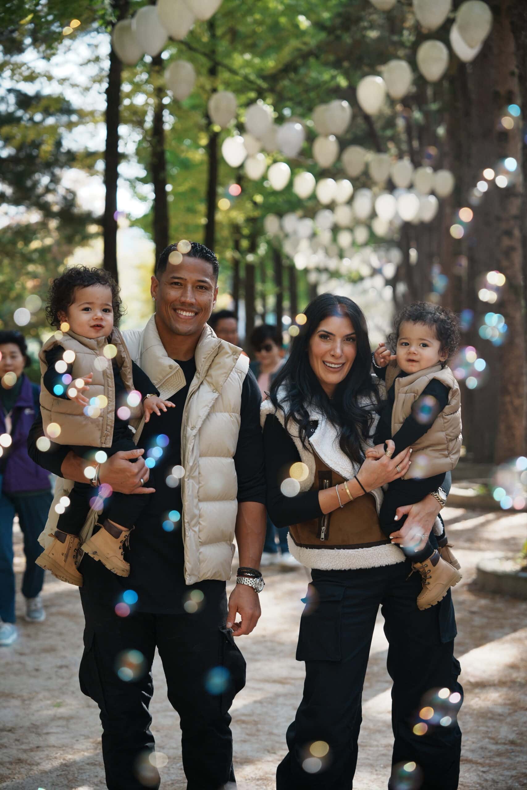 Family portrait of a multicultural family with two children at Korea photographers Goldenhour_MYM during a festival with lanterns and glowing bokeh lights, showcasing vibrant autumn colors and joyful moments.