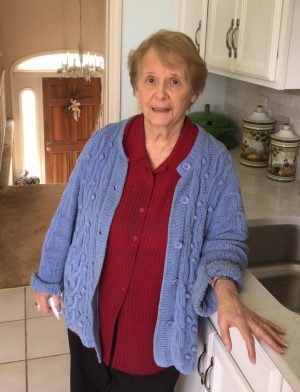 %Focuskw% | Good Tidings Plumbing, Heating &Amp; Cooling An older woman wearing a red shirt and blue cardigan stands in a kitchen, resting one hand on the counter and looking at the camera.