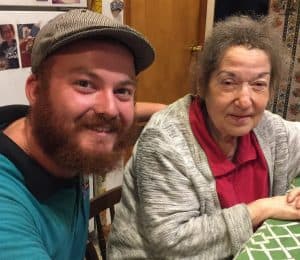 %Focuskw% | Good Tidings Plumbing, Heating &Amp; Cooling A man wearing a flat cap and a woman with gray hair sit together at a table, both looking at the camera and smiling.