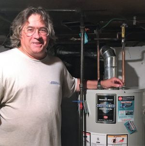 %Focuskw% | Good Tidings Plumbing, Heating &Amp; Cooling A man stands next to a Bradford White Defender water heater in a basement, smiling at the camera.