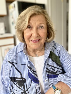 %Focuskw% | Good Tidings Plumbing, Heating &Amp; Cooling An older woman with short blonde hair, wearing a blue and white patterned shirt, smiles while seated indoors in a kitchen setting.