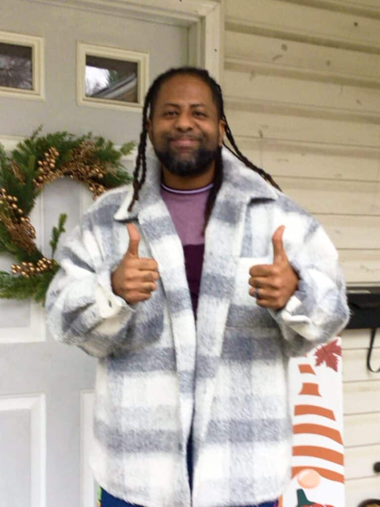 %Focuskw% | Good Tidings Plumbing, Heating &Amp; Cooling A man with long hair gives two thumbs up, standing in front of a white door decorated with a wreath. He is wearing a plaid jacket.