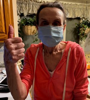%Focuskw% | Good Tidings Plumbing, Heating &Amp; Cooling An older woman wearing a face mask and a pink hoodie gives a thumbs-up gesture while standing in a kitchen.