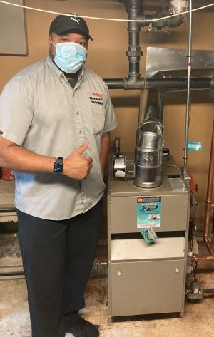 %Focuskw% | Good Tidings Plumbing, Heating &Amp; Cooling A technician wearing a mask and uniform gives a thumbs up next to a newly installed furnace in a utility room.