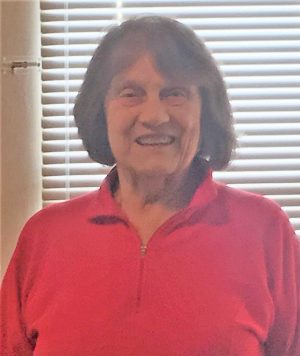 %Focuskw% | Good Tidings Plumbing, Heating &Amp; Cooling An older woman with short brown hair, wearing a red top, stands indoors in front of window blinds and smiles at the camera.