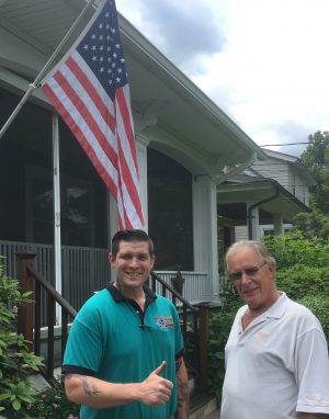 %Focuskw% | Good Tidings Plumbing, Heating &Amp; Cooling Two men stand outside in front of a house with a raised American flag. One man is giving a thumbs up and both are looking at the camera.