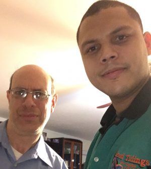 %Focuskw% | Good Tidings Plumbing, Heating &Amp; Cooling Two men stand indoors close together, one wearing glasses and a blue shirt, the other in a green collared shirt, both looking at the camera.
