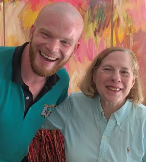%Focuskw% | Good Tidings Plumbing, Heating &Amp; Cooling A bald man and an older woman smile as they pose together in front of a colorful abstract painting.