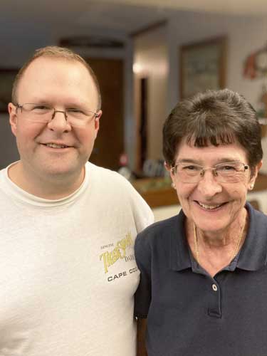 %Focuskw% | Good Tidings Plumbing, Heating &Amp; Cooling A man and an older woman stand side by side indoors, smiling at the camera. The man wears glasses and a white t-shirt; the woman has short dark hair and a navy shirt.