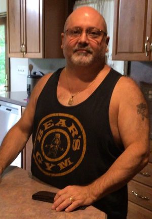 %Focuskw% | Good Tidings Plumbing, Heating &Amp; Cooling A middle-aged man with glasses and a beard stands in a kitchen, wearing a dark tank top that says "Bear's Gym.