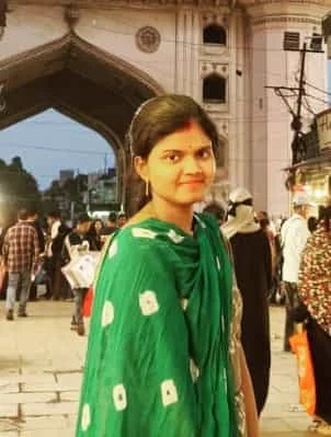 A woman in a green traditional outfit standing in front of Charminar in Hyderabad, surrounded by a bustling crowd, capturing the essence of the city's rich culture and vibrant atmosphere.