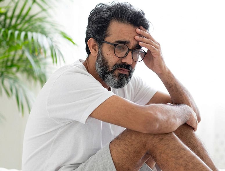 Man with gray hair and beard holding head in discomfort, male infertility concept.