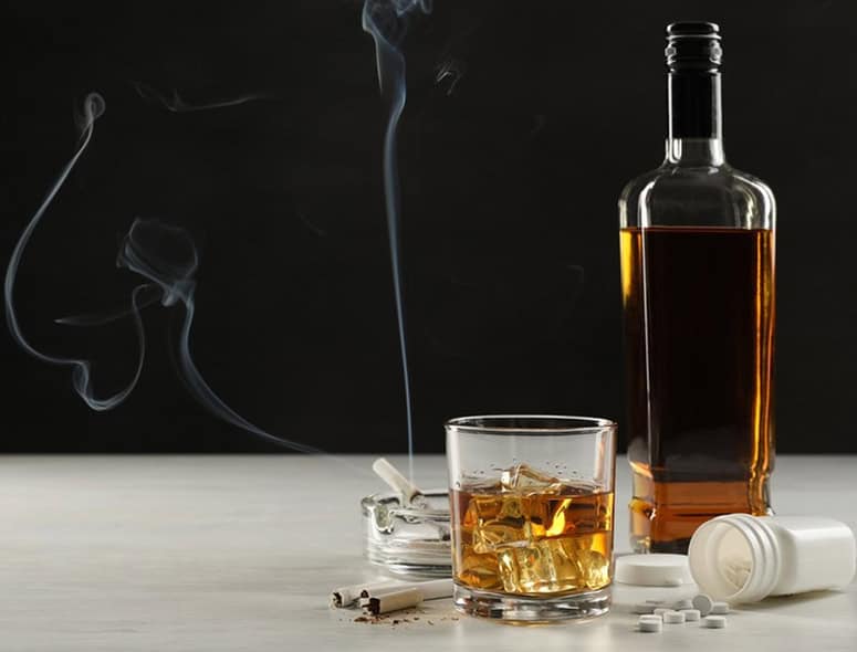 Alcohol and cigarette with smoke on dark background for health risks.