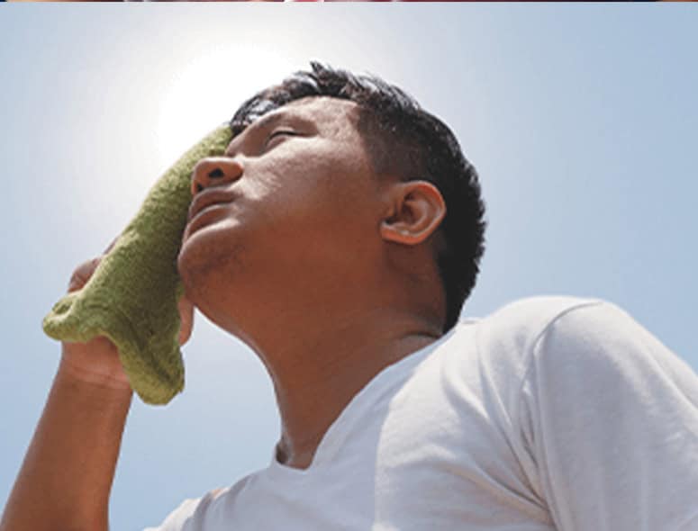 Man holding a green cloth to his ear, looking up outdoors under a clear sky.