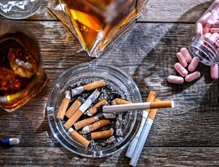 Ashtray with cigarette butts and alcohol bottles on wooden table.