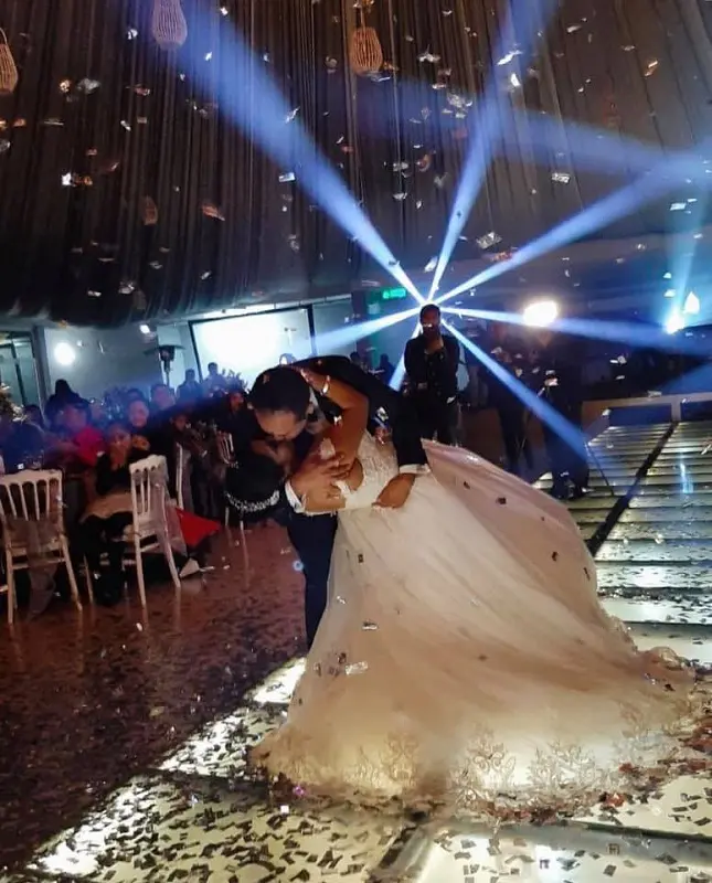 Andrea y Diego en su primer baile, con una pista iuminada y luces inteligentes de fondo. El la besa mientras la inclina hacia atrás en un gesto muy romántico