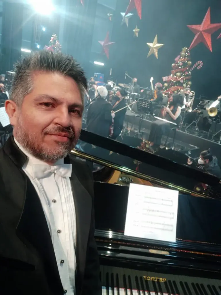 Miguel Gaytán, Director de Alfamusic, durante la grabación de un concierto de villancicos con los cantantes Emmanuel, Alexander Acha y José Luis Duval, sentado al piano de cola, vestido de frack con la orquesta al fondo