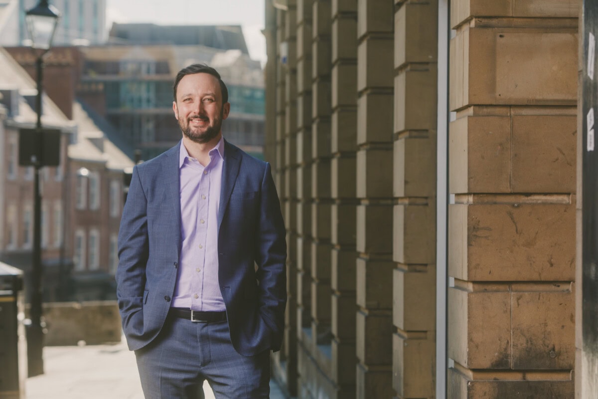 Confident businessman in a blue suit smiling outdoors in an urban setting.