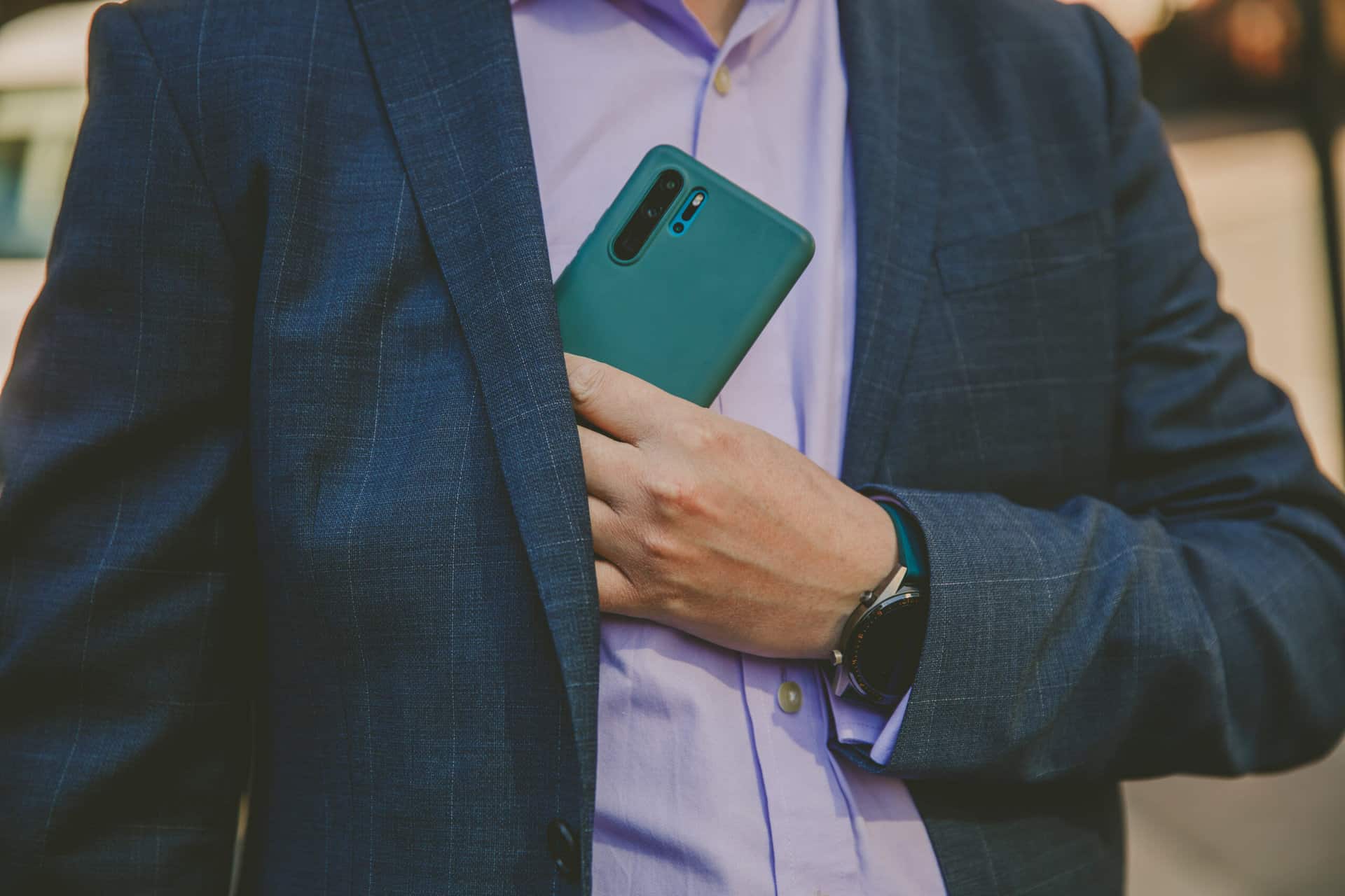 Holding smartphone in suit pocket, professional business man using mobile device outdoors.