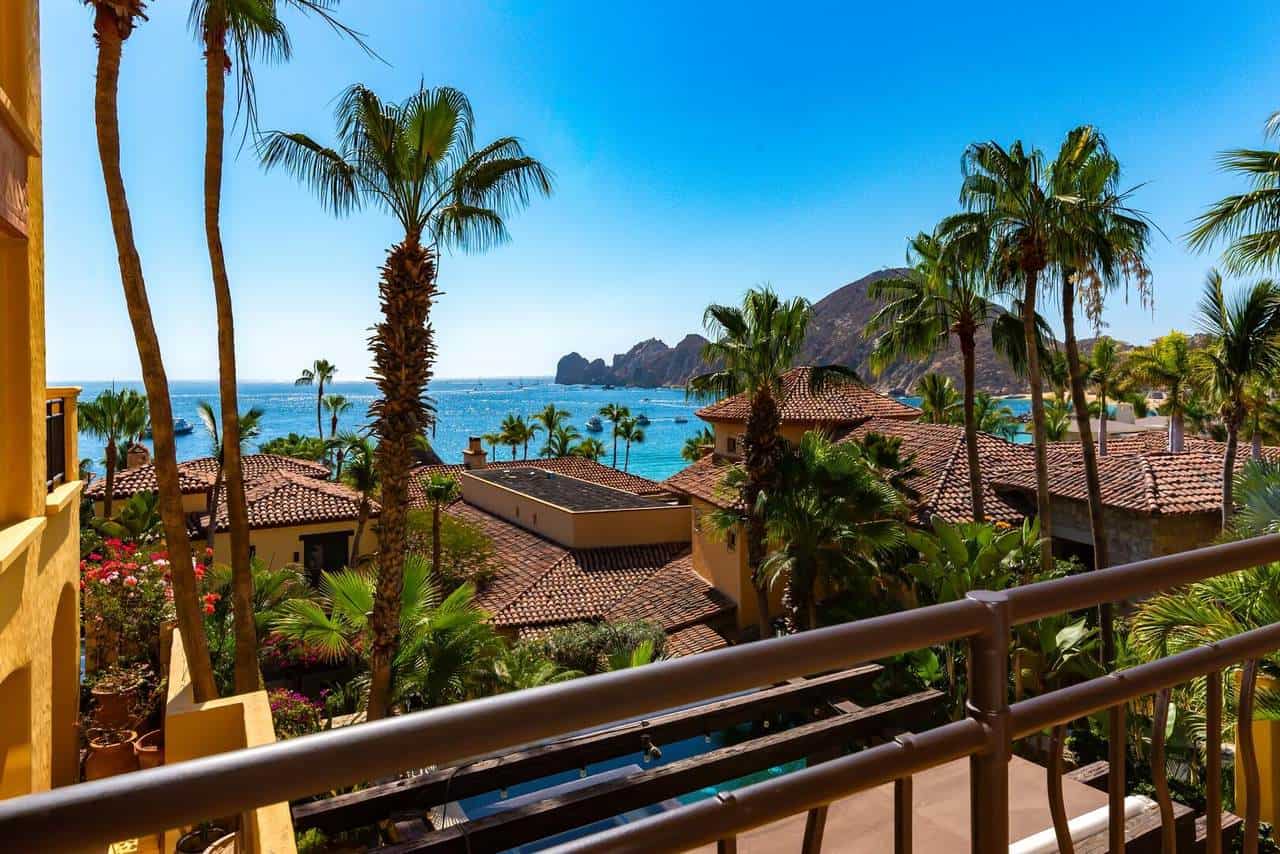 Stunning Ocean View From A Luxury Residence At Hacienda, Featuring Lush Palm Trees, Terracotta Rooftops, And A Clear Blue Sky Overlooking The Sea And Distant Mountains.