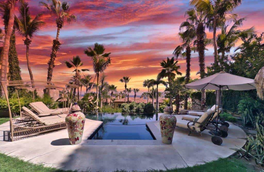 Stunning Pool Area At Sunset With Palm Trees, Lounge Chairs, And Vibrant Sky In Hacienda, Perfect For Luxury Real Estate Showcasing.